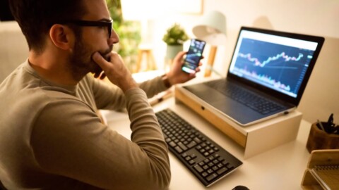 An investor looking at a chart on their computer screen while holding a smartphone.