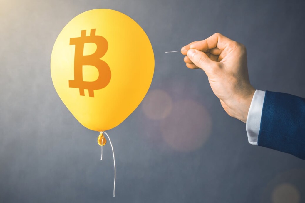 A balloon with a Bitcoin logo is approached by a hand holding a pin.