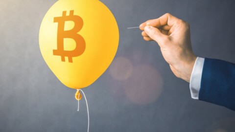 A balloon with a Bitcoin logo is approached by a hand holding a pin.